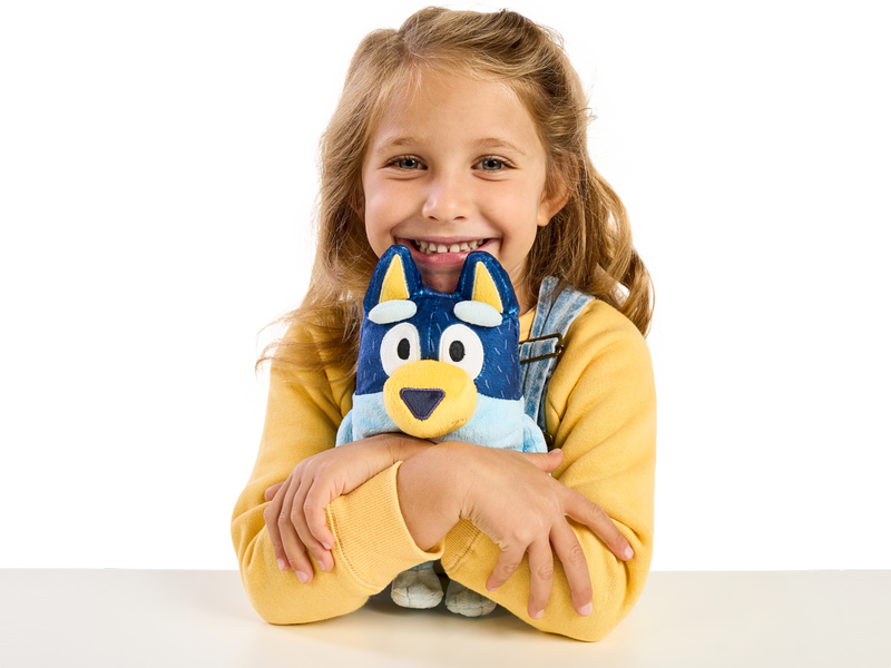 Young girl smiling and hugging a Bluey plush toy.