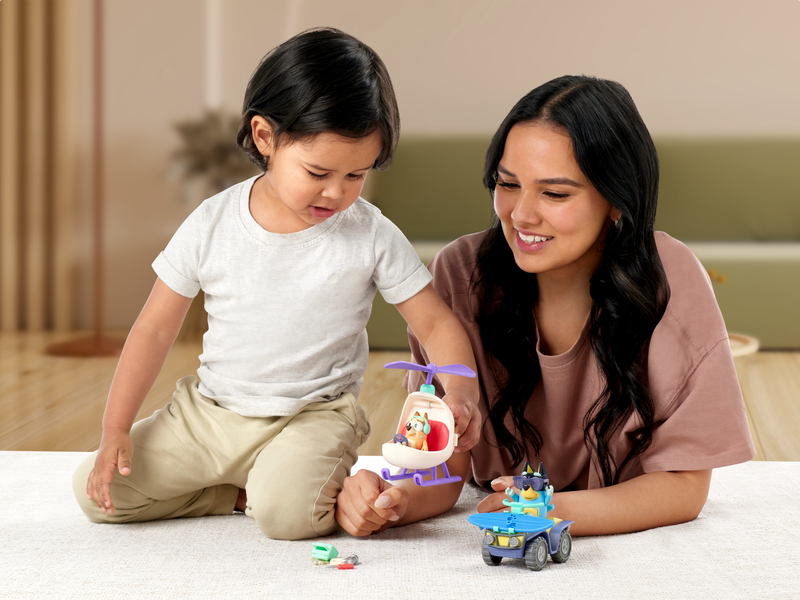 Mother and son playing with Bluey and Bingo figures in mini helicopter and cars.